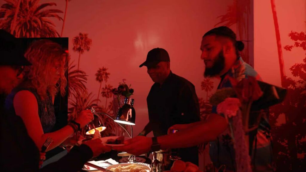 Three people interact at a buffet in a Planet Hollywood NYC event space bathed in red light, with palm tree silhouettes decorating the wall.