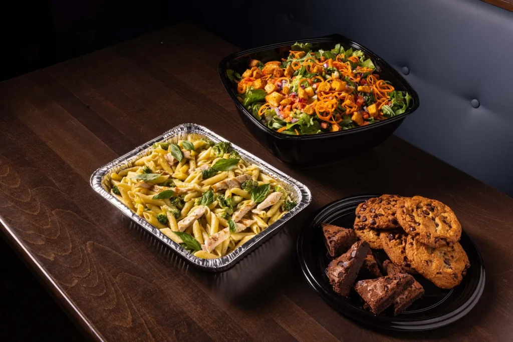 Planet Hollywood NYC catering menu featuring large trays of pasta, fresh salad, and delicious cookies.
