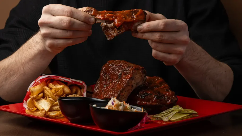 Signature BBQ ribs and fries being enjoyed by a guest at the Planet Hollywood NYC Times Square restaurant.