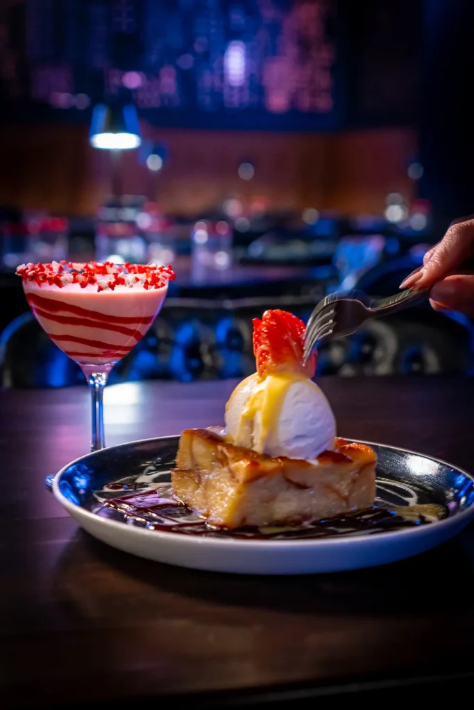 Blushing bread pudding with vanilla ice cream and strawberry topping, served with a Valentine’s cocktail.